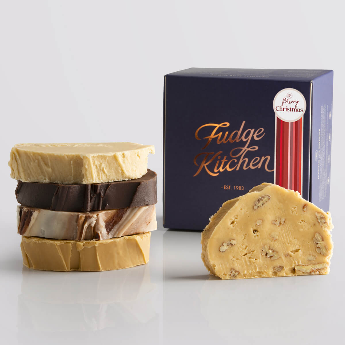 Vegan Slab Fudge Selection by Fudge Kitchen, features a collection of indulgent, handcrafted vegan fudge slabs in a variety of delicious flavours. Elegantly packaged in an indigo gift box and a Merry Christmas decorative seal, ideal for gifting or enjoying as a plant-based treat.