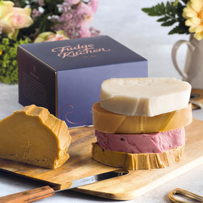 Caramel fudge and fruit fudge slices of fresh fudge are displayed on a board with a gilded gift box.