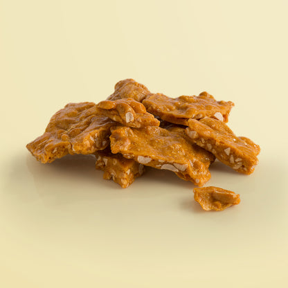 Close-up of the Peanut Brittle pieces by Fudge Kitchen, highlighting the golden, glossy texture of peanut brittle packed with roasted peanuts. A deliciously crunchy treat for nut enthusiasts.